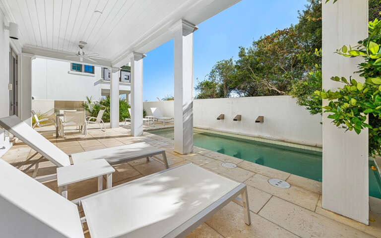 Relax poolside in your private oasis, where white loungers await under elegant columns and lush greenery surrounds your tranquil retreat.