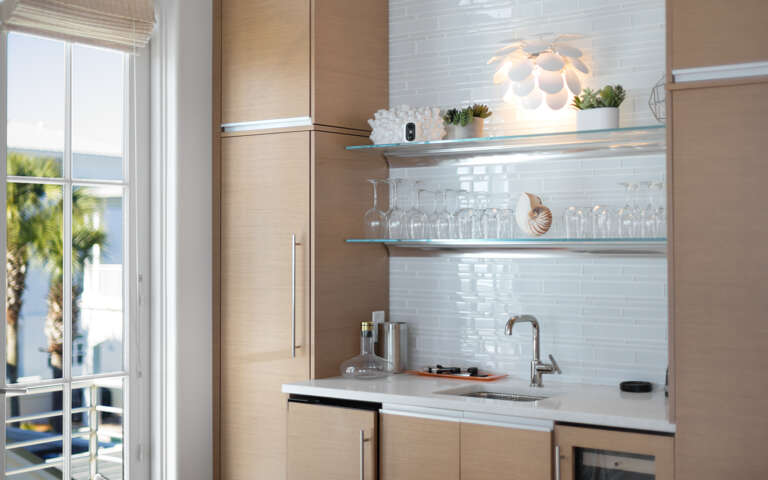 Your stylish kitchenette features modern appliances and elegant glass shelving, perfect for preparing meals with views of swaying palms.