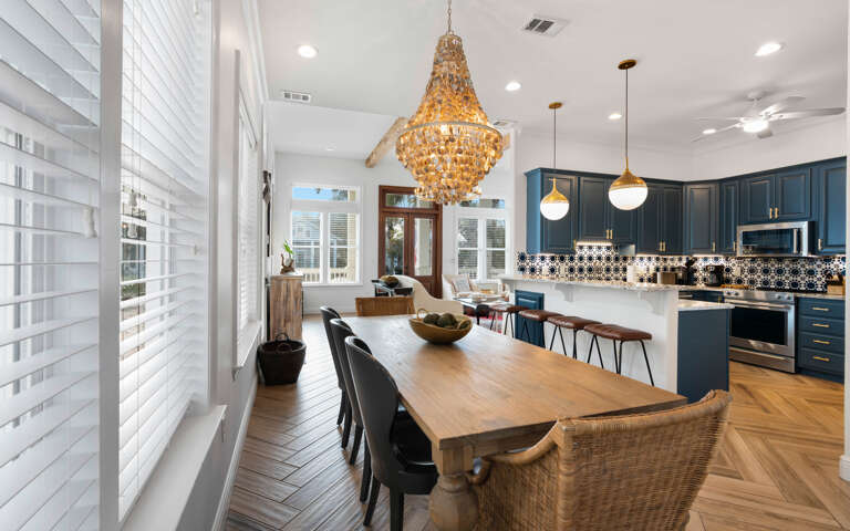 Your open-concept kitchen and dining space gleams with rich navy cabinets, elegant chandeliers, and warm hardwood floors perfect for gathering.