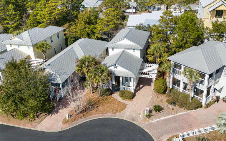 Aerial view of charming coastal cottages with metal roofs nestled among palm trees and tropical landscaping in a peaceful residential community.