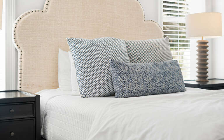 Sink into this serene bedroom where crisp white linens meet stylish patterned pillows, creating your perfect retreat for restful nights.