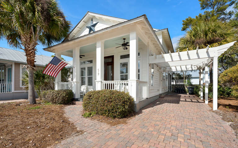 This charming coastal home features classic architecture with white columns and decorative star details, surrounded by tropical palms and mature landscaping.