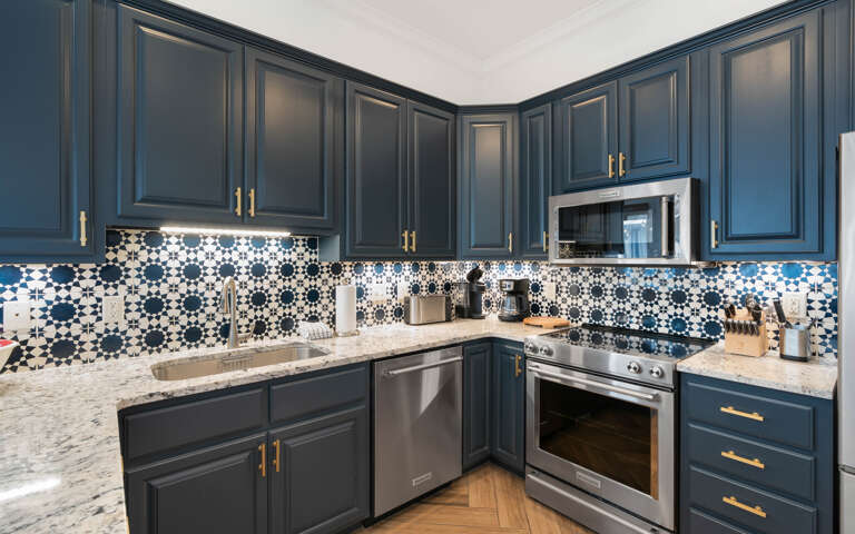 Your stylish kitchen features navy cabinetry, marble countertops, and stunning patterned tile backsplash, fully equipped for cooking memorable meals.