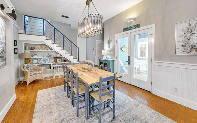Gather around your stylish dining table beneath the statement chandelier, with warm hardwood floors and charming coastal touches creating the perfect space for memorable meals.