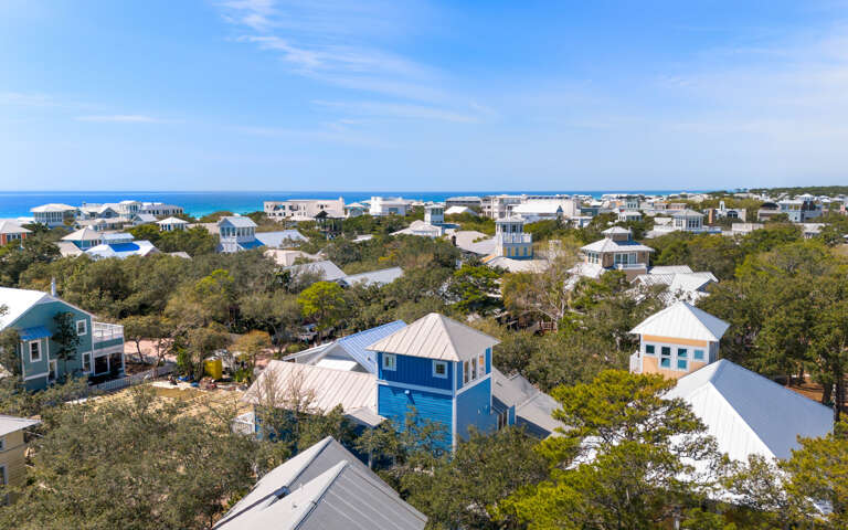 Aerial view showcases the scenic coastal community with charming beach houses nestled among lush trees, just steps from pristine blue waters.