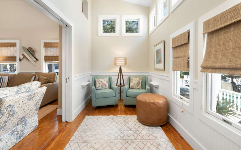 Your peaceful reading nook awaits with twin seafoam chairs, warm leather ottoman, and natural light streaming through bamboo shades.