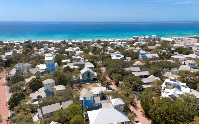 Charming coastal community overlooking pristine turquoise waters and white sandy beach, surrounded by lush vegetation.