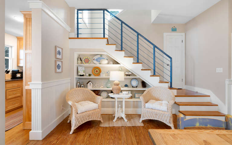 Cozy reading nook beneath the stairs invites you to curl up in wicker chairs with a good book and coastal décor.