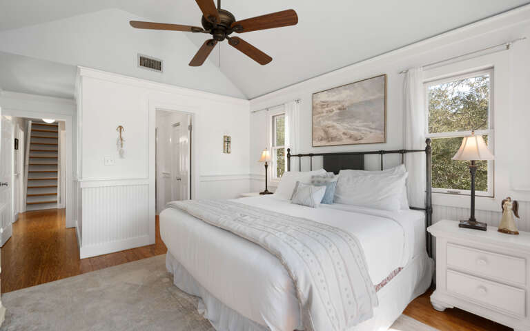 Unwind in your peaceful bedroom featuring crisp white linens, warm wood floors, and a gentle ceiling fan overhead.