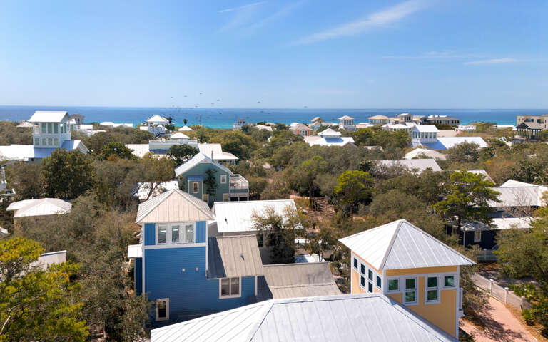 Coastal community with colorful beach houses nestled among mature trees, offering stunning ocean views and peaceful seaside living.