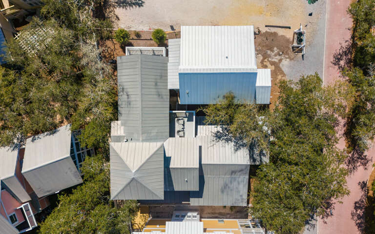 Aerial view of the modern property showcasing distinctive architecture with white metal roofing and blue accents nestled among mature trees.
