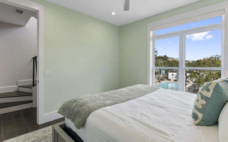 Drift off in this serene bedroom where soft green walls and crisp linens create your perfect retreat, with pool views beyond.