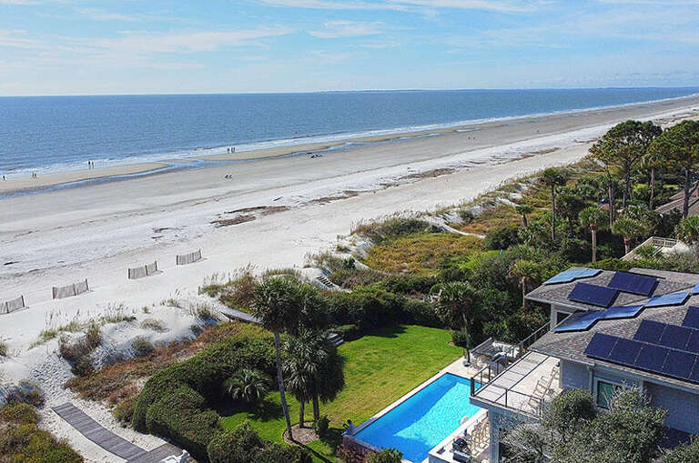 Aerial View Of Seaside Structure With Pool Adjacent To Expansive Beach