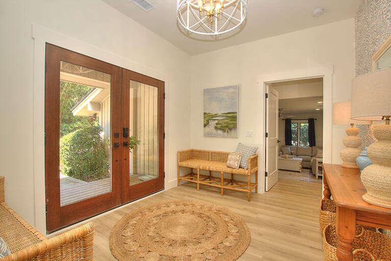 Bright Entryway With Bench, Round Rug, And Open Doors Leading Into A Spacious Room