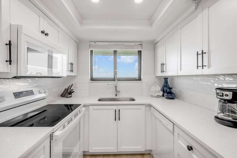 Renovated kitchen with fresh white appliances, cabinets, and countertops—fully equipped for your beach getaway
