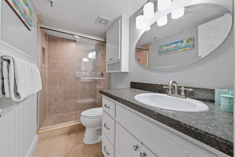 The guest bathroom has a glass and tile shower and white spa towels