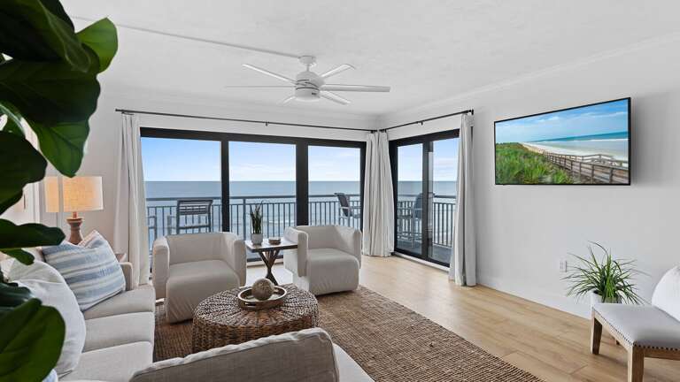 Relax in the oceanfront living room, featuring a mounted cable TV for your entertainment while enjoying the stunning views of New Smyrna Beach