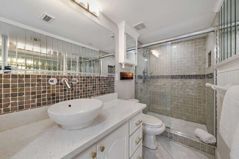 The guest bathroom features a glass and tile shower with plush spa towels