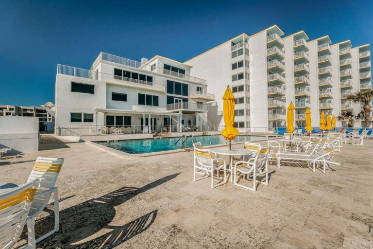 The beachfront pool deck features a seasonally heated pool, along with tables, chairs, and umbrellas for relaxing, plus a conveniently located clubhouse