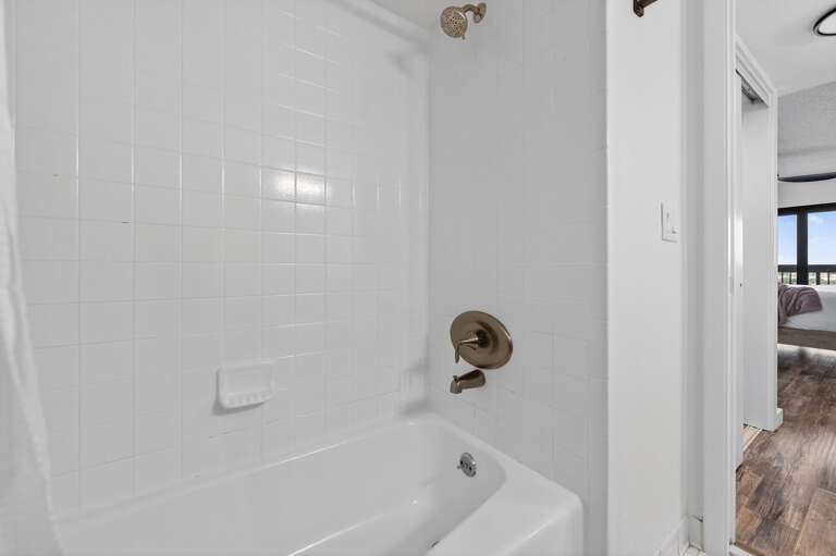 The bathroom features a stylish tile tub/shower combo and plush spa towels for a relaxing, beach-ready refresh