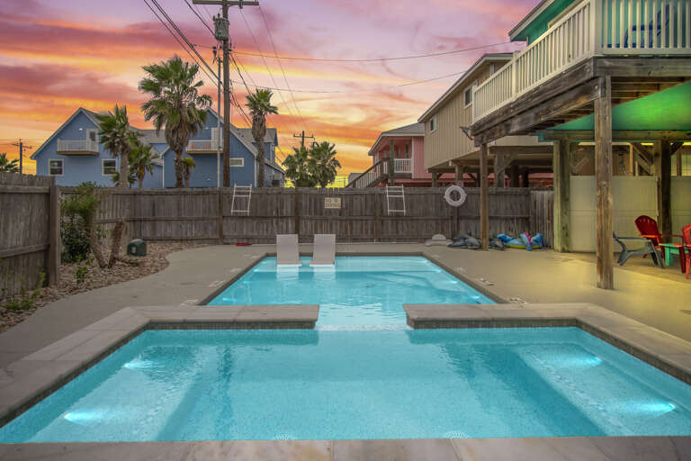 Swimming Pool At Dusk With Surrounding Buildings And Palm Trees