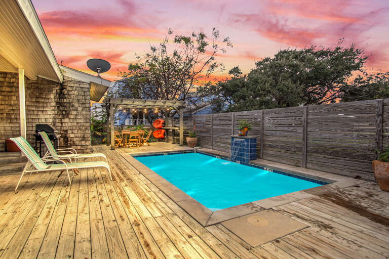 Backyard With Swimming Pool And Wooden Deck At Sunset