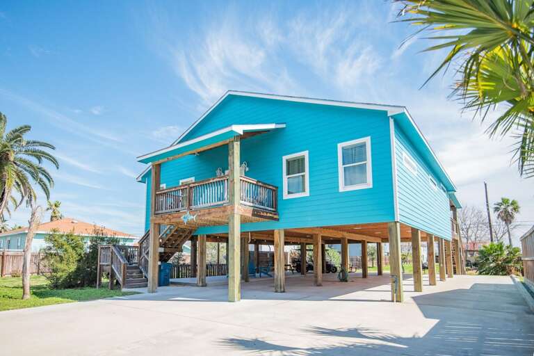 Blue Elevated House With Balcony And Palm Trees