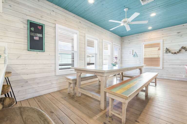 Interior Dining Area With Wooden Table And Benches, White Walls, Ceiling Fan, And Windows