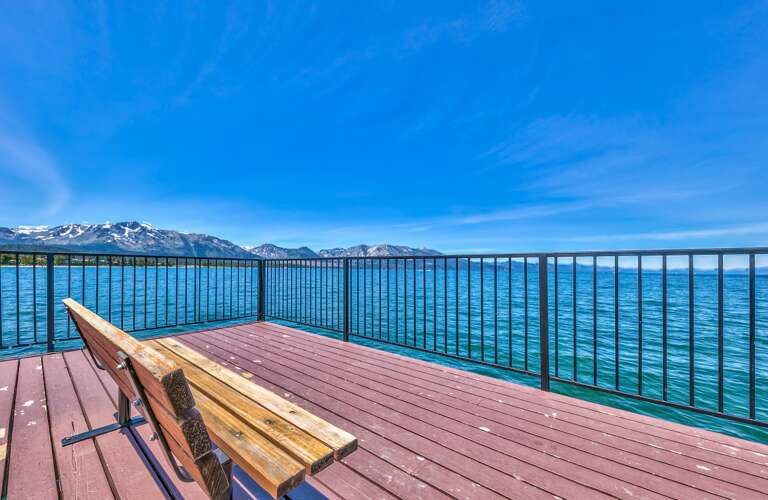 Lakefront Deck And Bench, Blue Waters And Mountain Backdrop