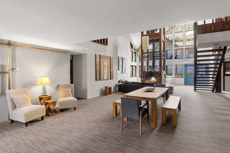 Spacious Living Area With Tall Windows, Wooden Staircase, And Dining Table