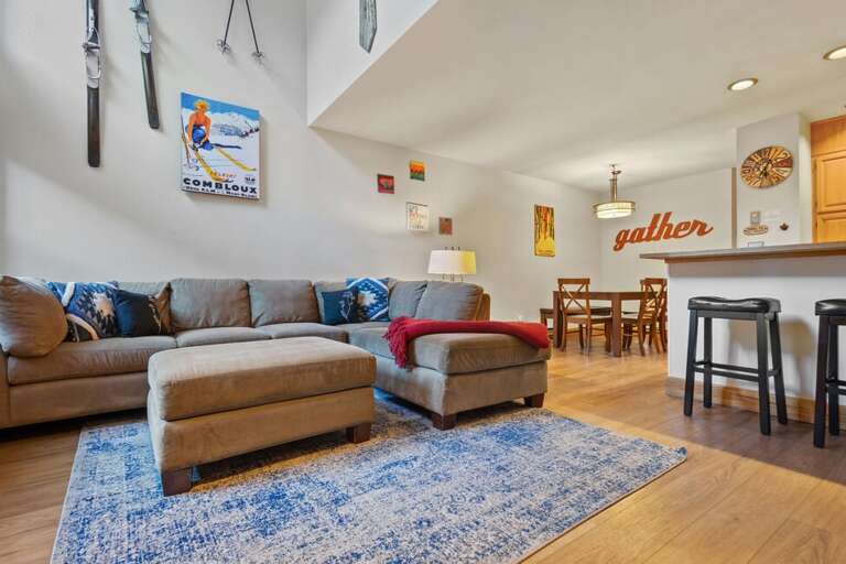 The condo's open living area features a huge L-shaped couch that flows seamlessly into the kitchen and dining space, creating a bright, connected space for relaxing and entertaining.