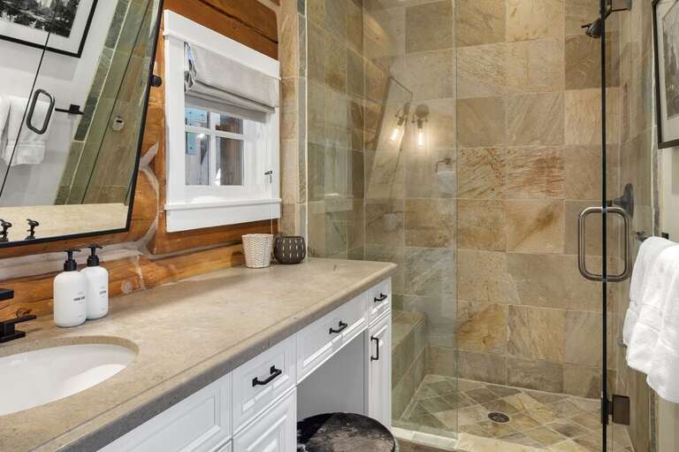 The ensuite features a tiled step-in shower with a bench and a spacious vanity, combining modern elegance with guest comfort