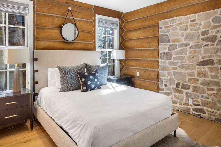 The first of the guest rooms features a queen bed with a modern cabin aesthetic and a private ensuite bathroom, thoughtfully located off the main level for comfort and privacy.