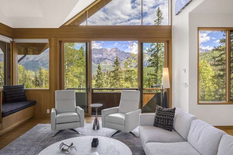 A stunning living room with cozy modern seating offers breathtaking mountain views through expansive windows that flood the space with natural light.