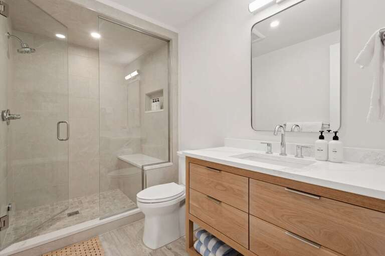 Primary ensuite features step in tiled shower with seating bench and single vanity.