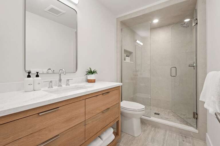 shared bathroom features step in tiled shower and single vanity.