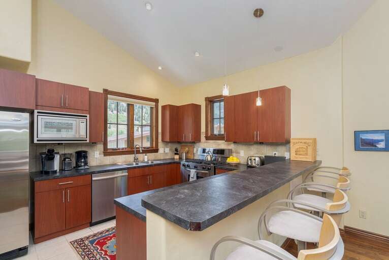 Open kitchen overlooking living area, features stainless steel appliances, plenty of counter space for entertaining and counter seating for 4.