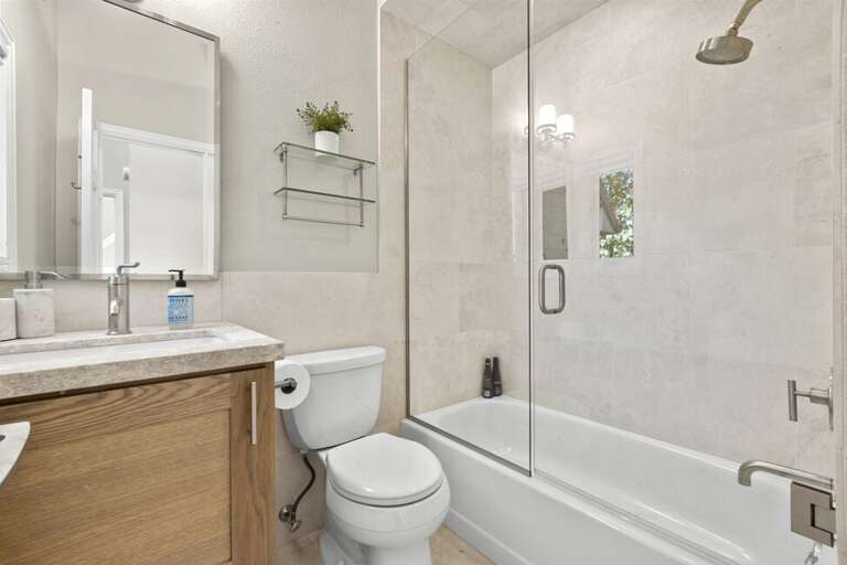 The second bathroom features a step-in tub and shower combo, a single vanity, and natural light, creating an open and clean feel.