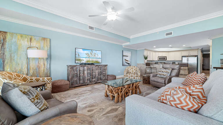 Spacious Living Space With Light Blue Walls, Plush Sofas, And A Wooden Coffee Table, Blending Into A Kitchen Area