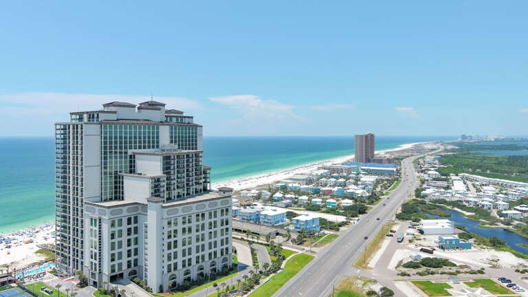 Aerial View Of A Beachfront High-rise Building Near A Coastal Road