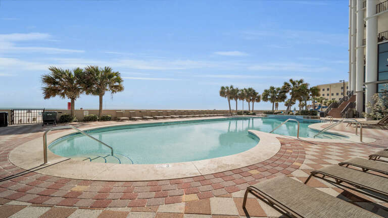Outdoor Swimming Pool By The Sea With Palm Trees And Lounge Chairs