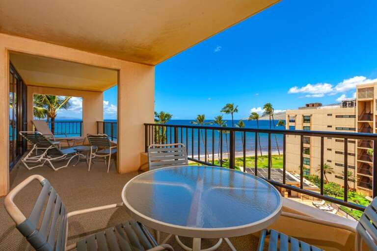 Balcony View Of Beachfront Vacation Rental With Table And Chairs Overlooking Palm Trees And Buildings