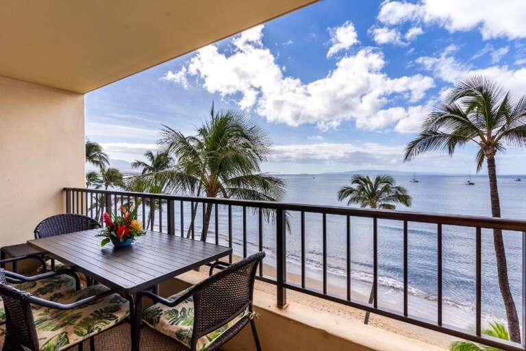 Balcony View Of Beach With Palm Trees, Patio Furniture, And Ocean In The Background