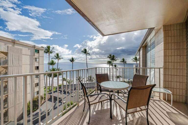 Balcony View Of Blue Sea Between Buildings With Table And Chairs Under Shade