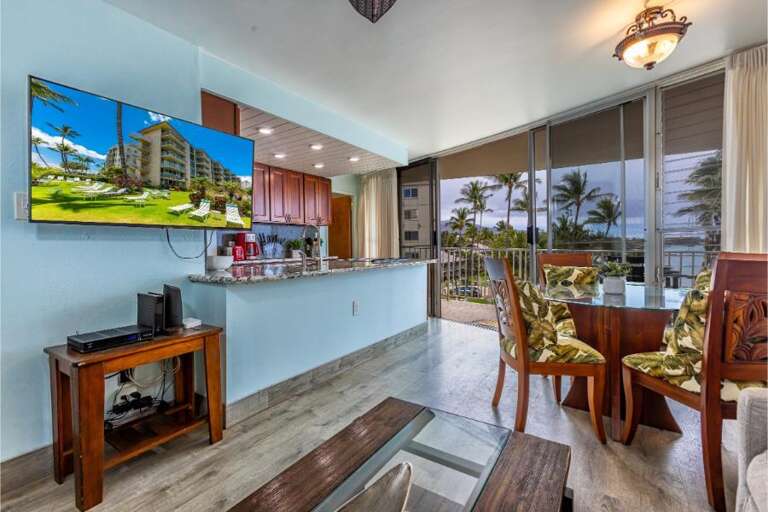 Interior View Of A Vacation Rental, Showcasing A Living Area With Television Leading To A Balcony With Palm Tree Views