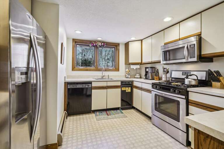 This kitchen has an electric stove, microwave, dishwasher, coffee pot.