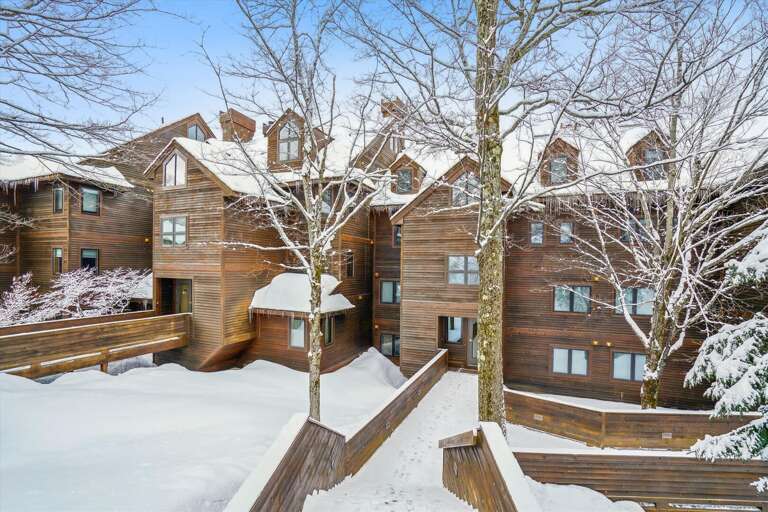 Snowy Scene Showing A Series Of Staggered Wooden Buildings Nestled Among Bare Trees