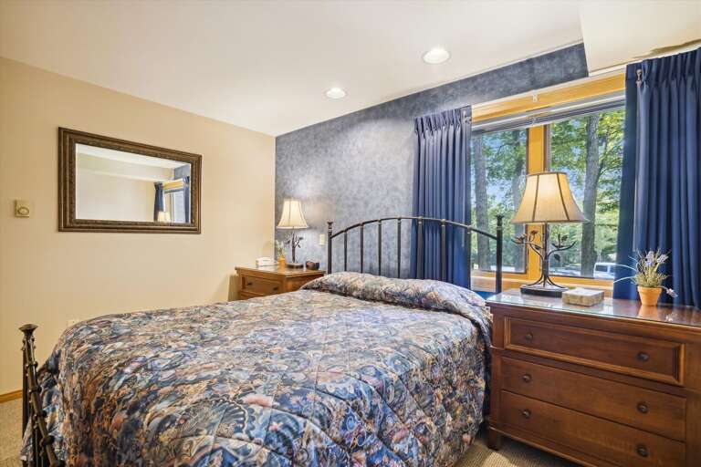 Beautifully adorned queen bedroom with large windows which frame the nature scene surrounding Highridge