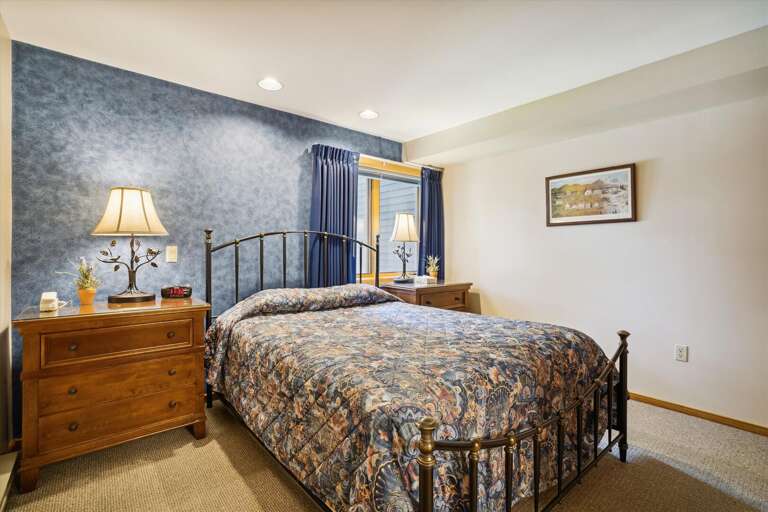 Beautifully adorned queen bedroom with large windows which frame the nature scene surrounding Highridge