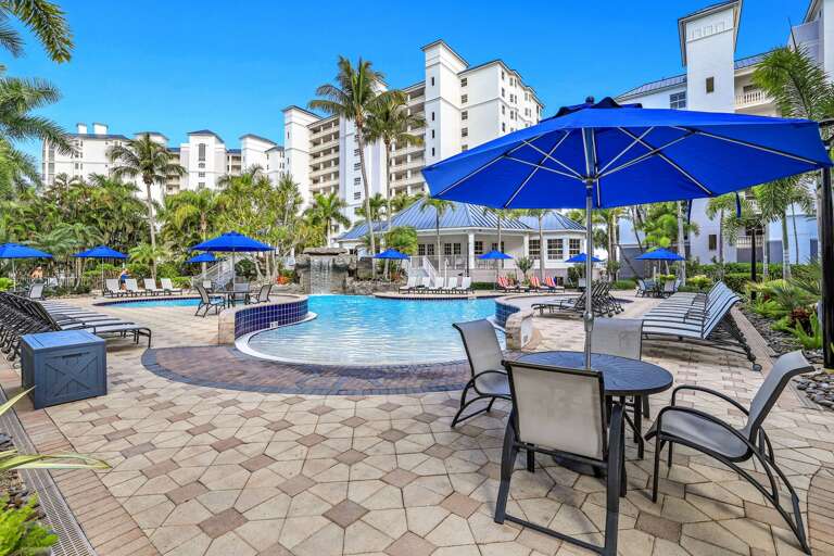 Blue Umbrellas, Palm Trees, Poolside Chairs, And Tiled Terrace